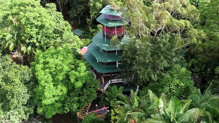 An aerial image of a tall colourful tower with green tin rooves amidst a forest