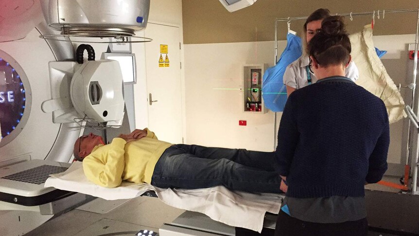Prostate cancer patient Russell Flack lies down on a medical scanning machine, with two medical technicians looking on