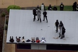 Aerial vision of police in riot gear on top of a roof at Banksia Hill Detention Centre, multiple detainees lying on stomachs.
