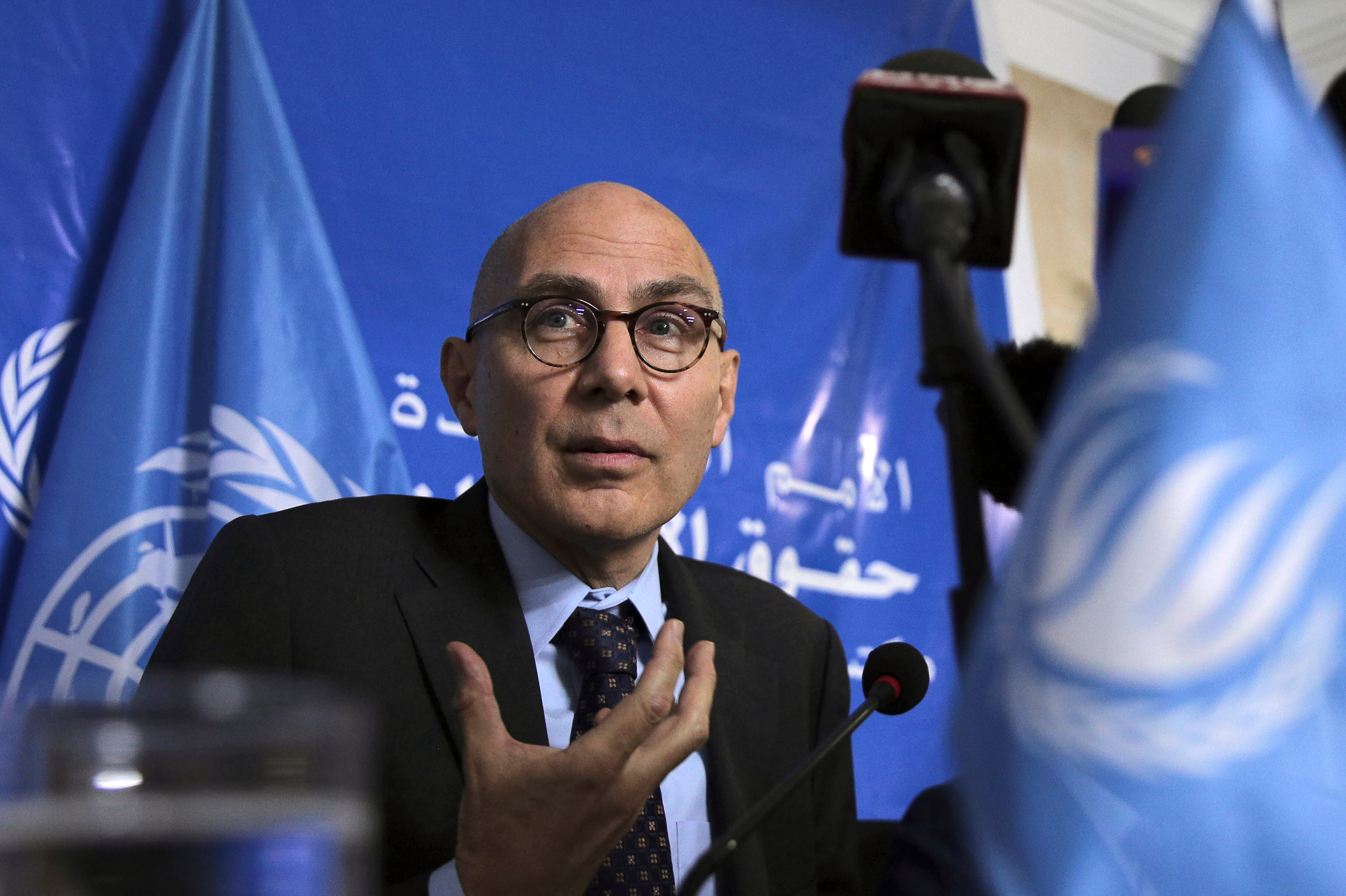 Volker Turk está sentado com uma mão levantada em frente a um fundo azul.