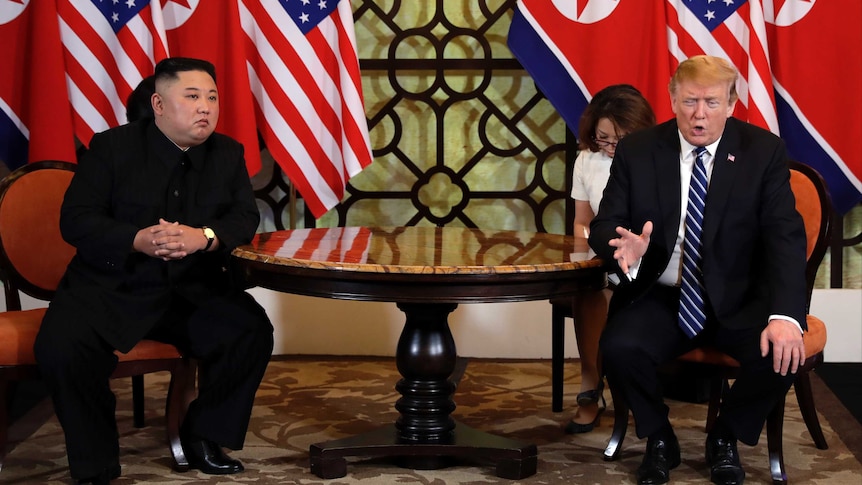 Kim Jong-un, with his hands clasped, sits next to Donald Trump who is gesturing with his hand as he speaks.