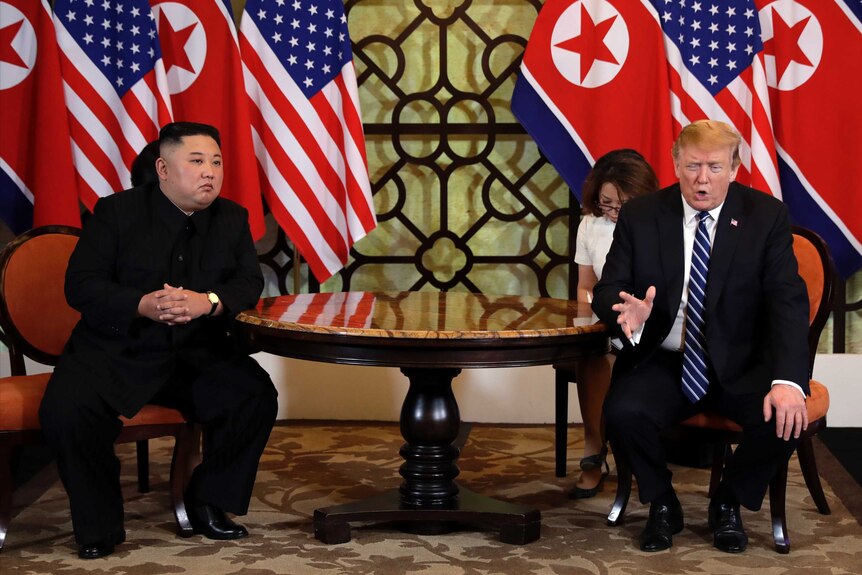 Kim Jong-un, with his hands clasped, sits next to Donald Trump who is gesturing with his hand as he speaks.