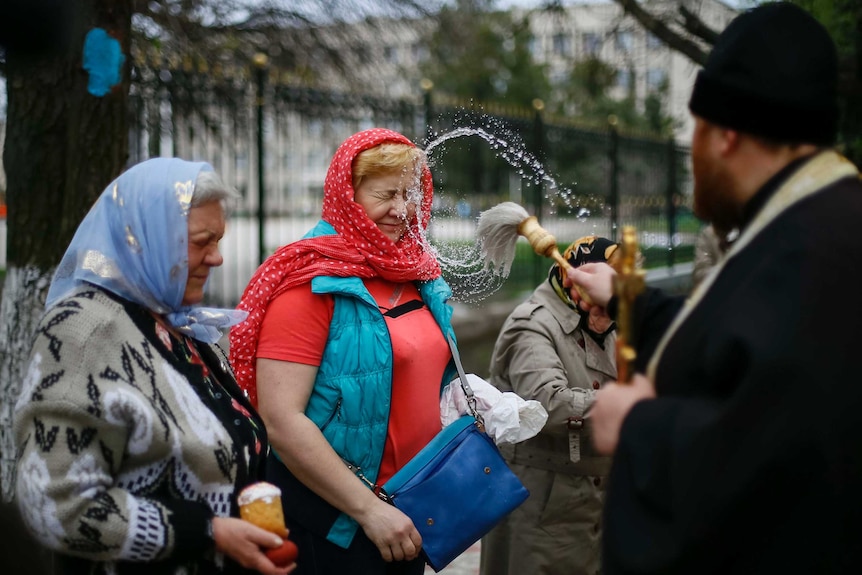 A Ukrainian orthodox priest throws holy water on two women in headscarves