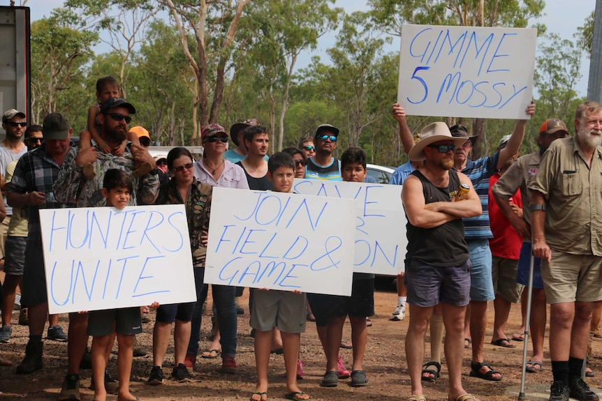 A number of people hold up signs with slogans protesting limits on hunting.