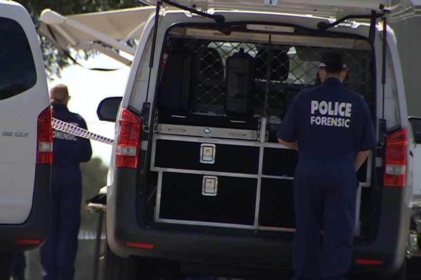 A police officer in blue overalls with the words 'police forensic' written in white, looks in the back of a white van.