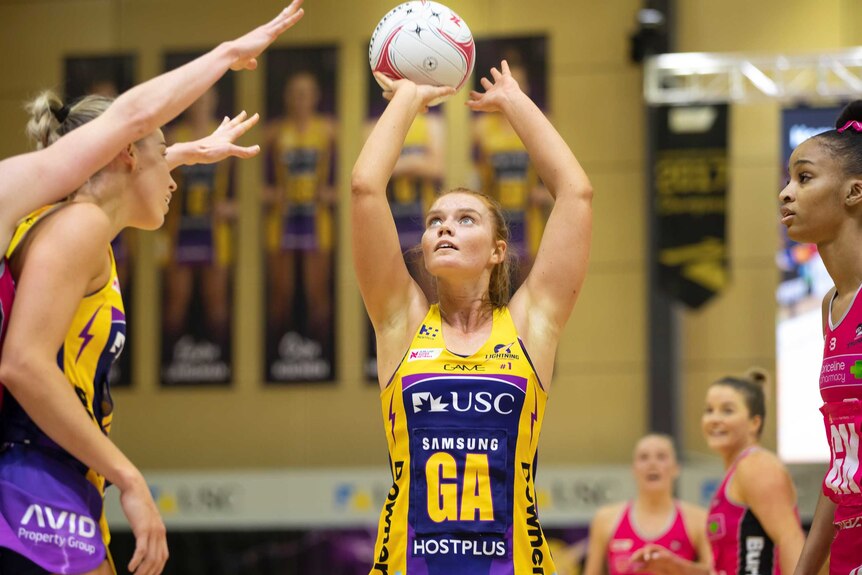 A netball player holds the ball above her head ready to take a shot at goal.