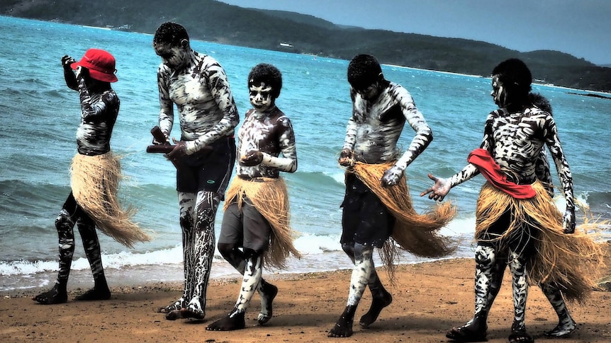 A group of boy walk along the beach dressed in traditional dress.