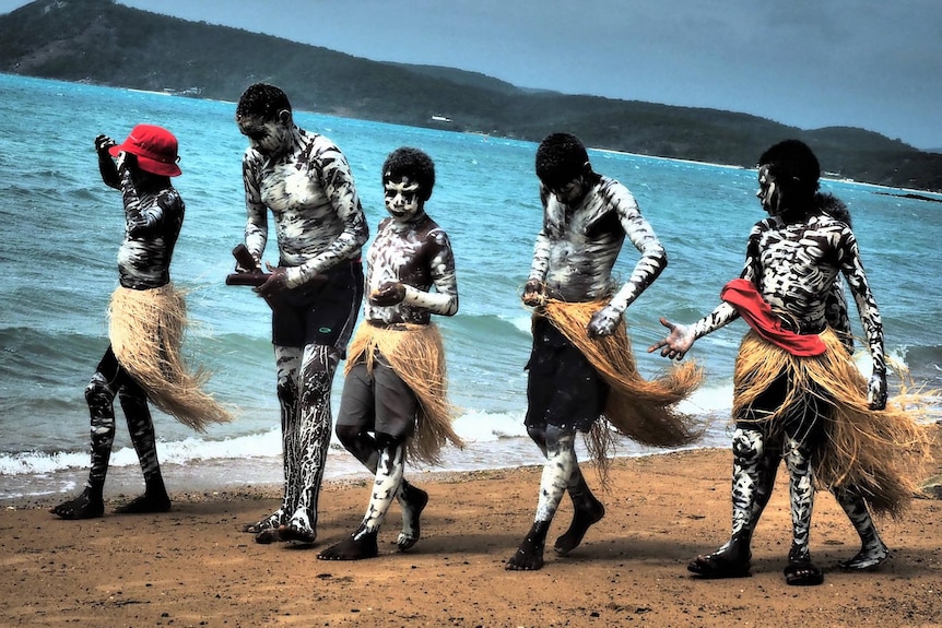 A group of boy walk along the beach dressed in traditional dress.
