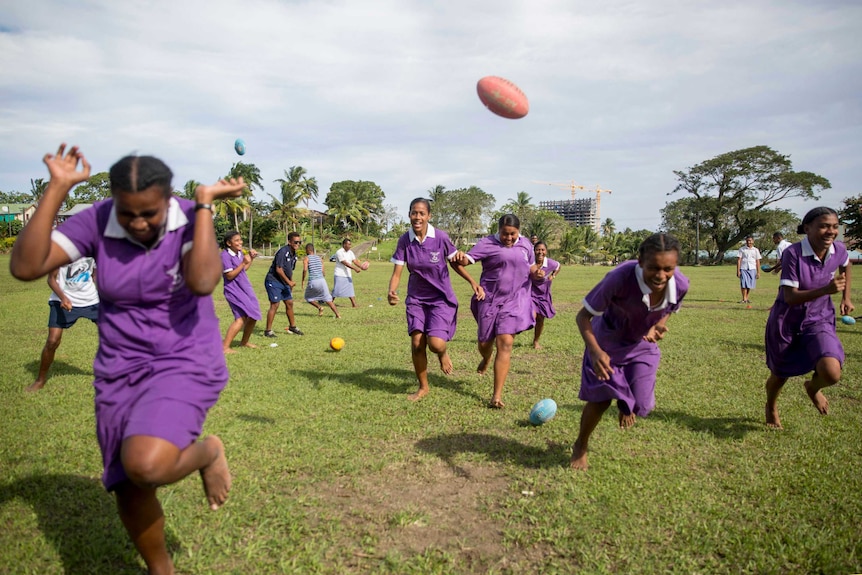 Fijian girls run through a gauntlet of footballs, ducking and laughing