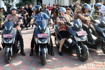 Lines of black motorbikes with drivers, men and women wearing help facing the camera.
