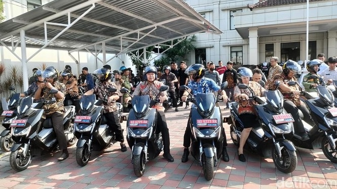 Lines of black motorbikes with drivers, men and women wearing help facing the camera.