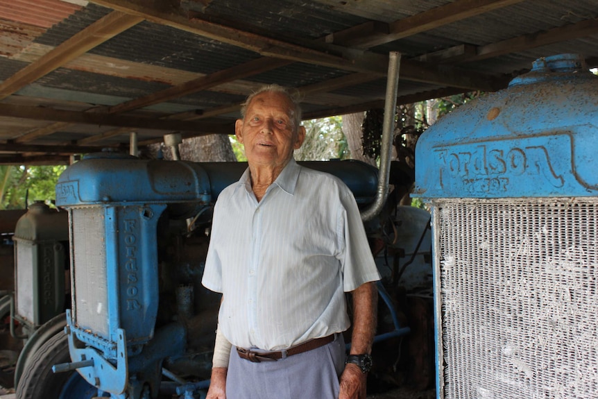 A man standing in between two old blue tractors and smiling.