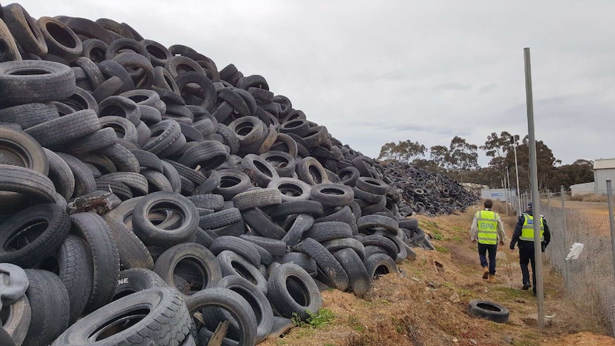 A man in an EPA high vis vest and a police officer walk past an enormous pile of tyres.