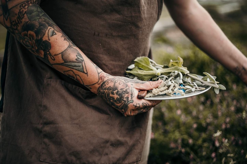 Chef clutches a plate of herbs and a knife