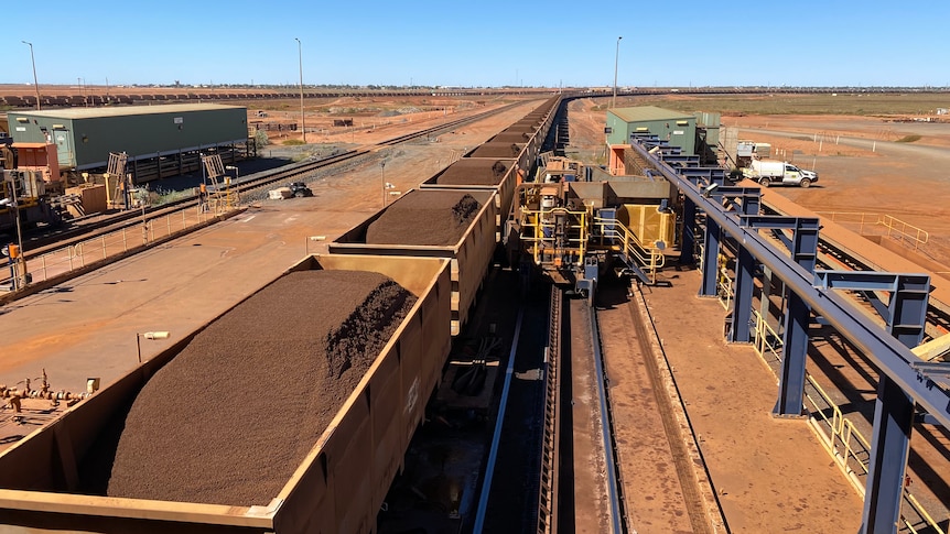 Fortescue Metals iron ore train cars sit alongside machinery.