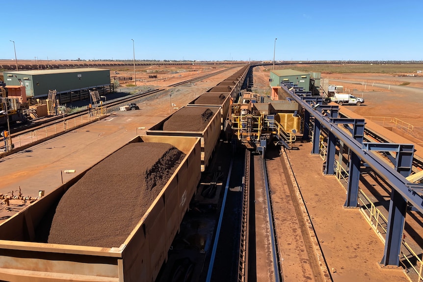 Los vagones de tren de mineral de hierro de Fortescue Metals se encuentran junto a la maquinaria.