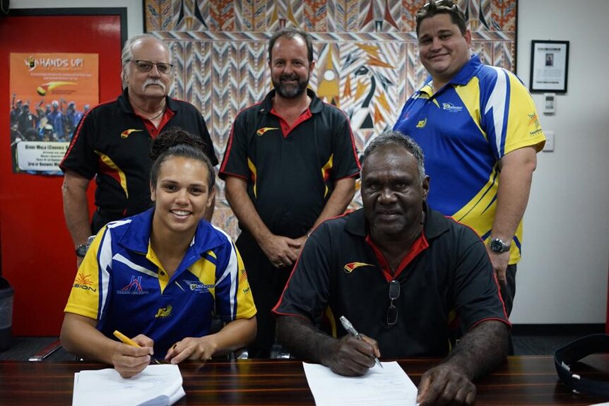 A group of people signing documents and smiling.