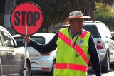 Rodney James in sun hat and fluoro vest holds a stop sign at a school crossing