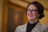 A woman with black hair and glasses wearing a checked jacket