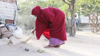 A woman wearing a red cape bends down to pick up something from the ground.