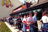 Dozens of people dressed in summer clothing queue outside a McDonald's restaurant
