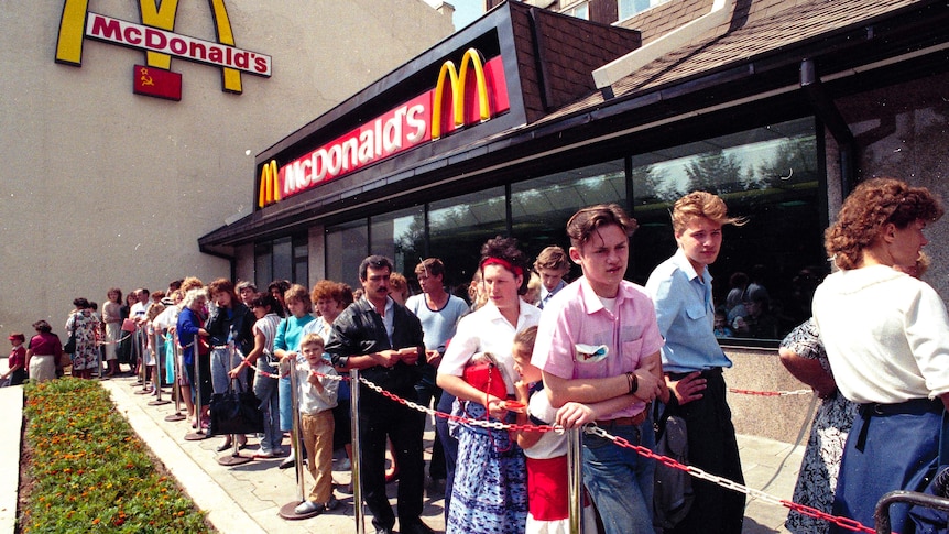 Dozens of people dressed in summer clothing queue outside a McDonald's restaurant