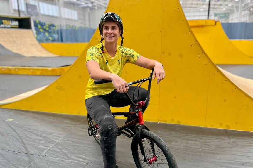 A woman sits on a BMX bike inside a ramp track