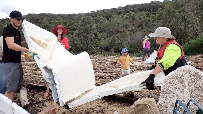 Three volunteers, a man and two women, carry a large piece of cladding left on Patonga Beach after the Hawkesbury floods 2022.