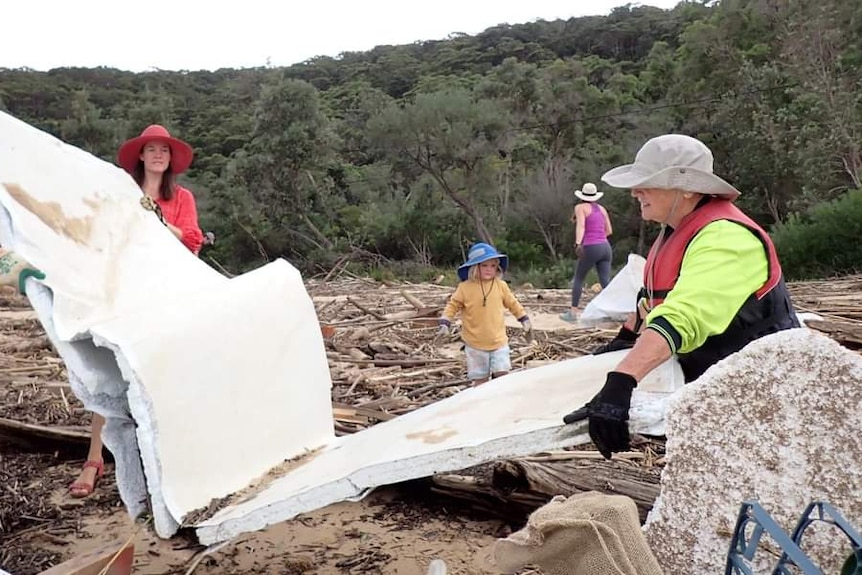 Three volunteers, a man and two women, carry a large piece of cladding left on Patonga Beach after the Hawkesbury floods 2022.