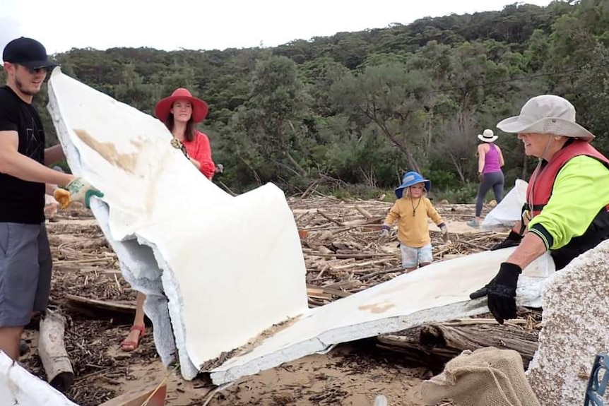 Three people collect a large piece of cladding, washed up on the Patonga Beach in flooding. March 2022