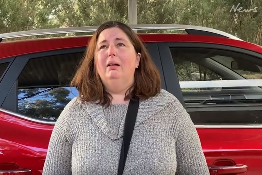 A woman cries in front of a car.