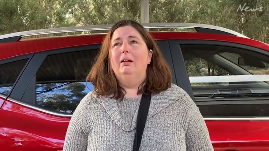 A woman cries in front of a car.