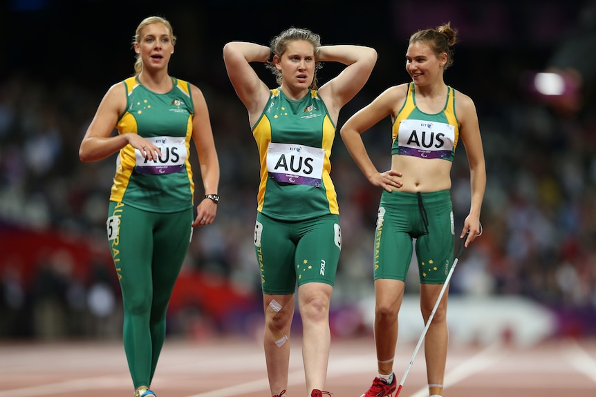 Three women in green and gold athletic wear on a running track