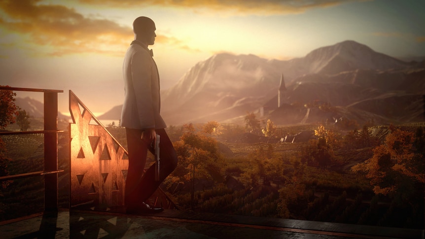 Screenshot from Hitman 3, with the titular assassin in a white tux, holding a gun, looking at mountains in the distance.