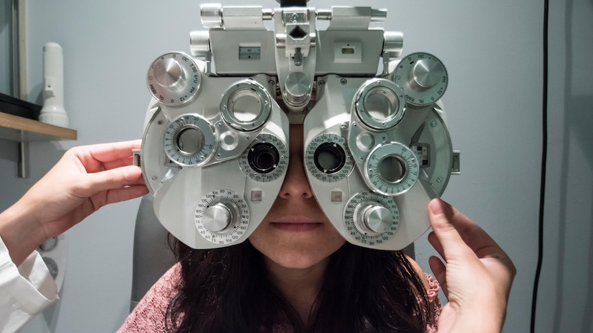 An optometrist adjusts a machine over a woman's face