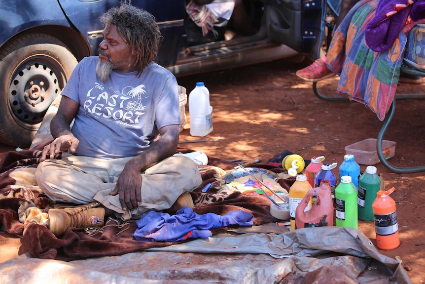 Indigenous artist homeless next to his paint supplies.