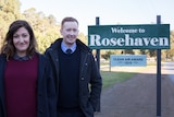 Celia Pacquola and Luke McGregor pose next to a sign that says 'Welcome to Rosehaven'