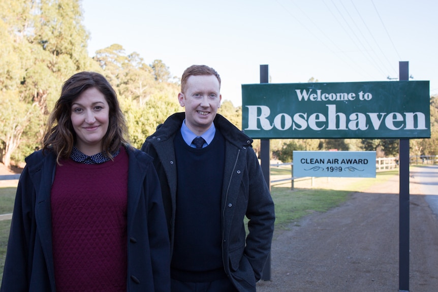 Celia Pacquola and Luke McGregor pose next to a sign that says 'Welcome to Rosehaven'