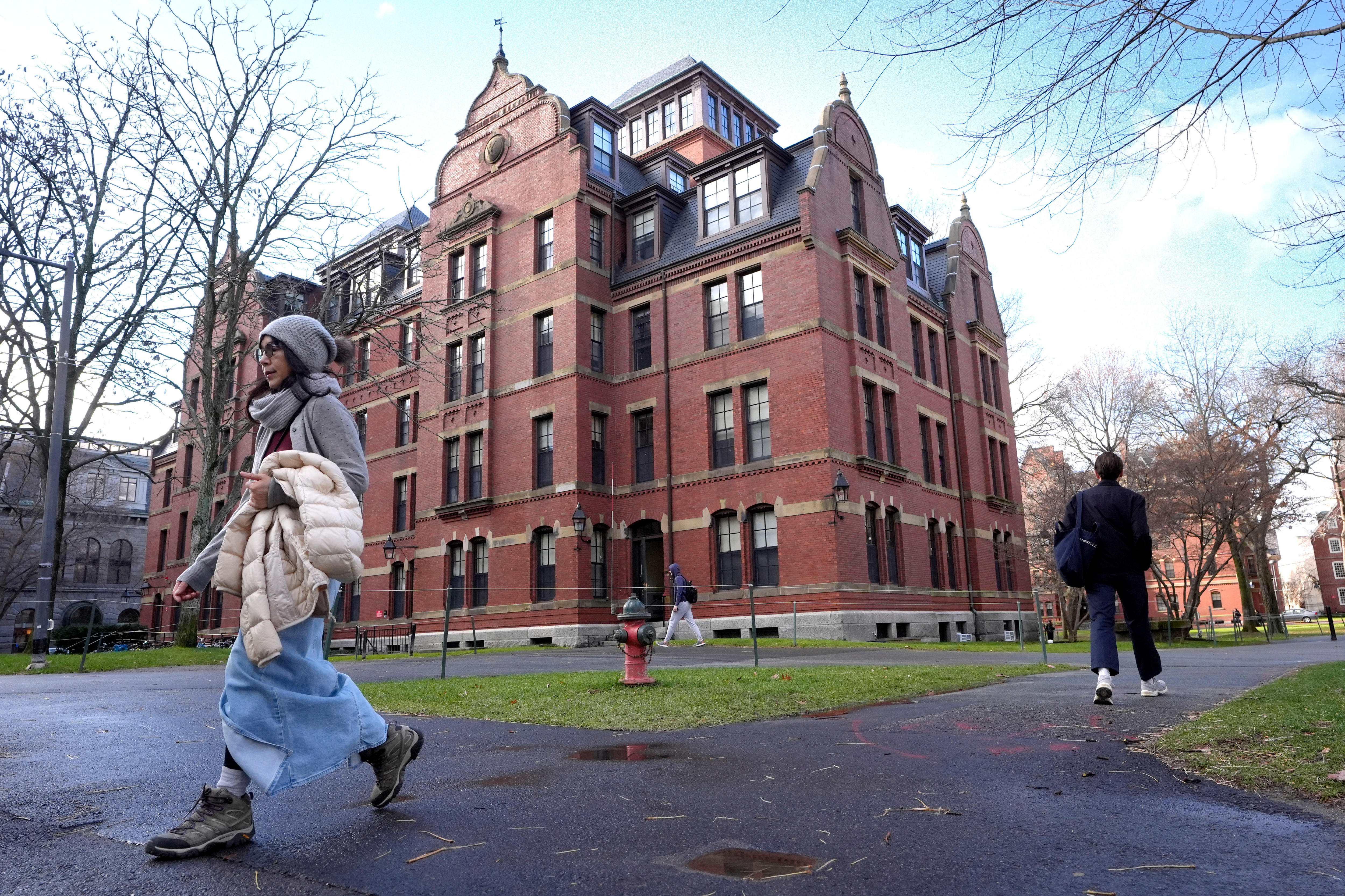 People walking past a red stone building on Harvard's campus. 