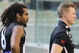 Collingwood coach Nathan Buckley stands in front of Heritier Lumumba on the sideline of an AFL game.