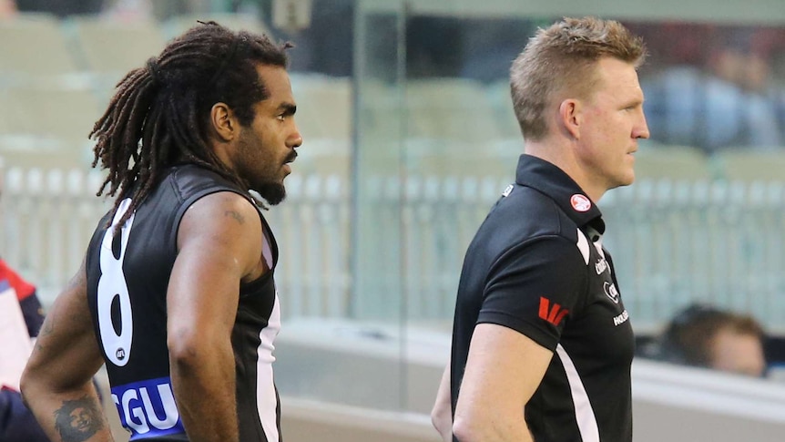 Collingwood coach Nathan Buckley stands in front of Heritier Lumumba on the sideline of an AFL game.