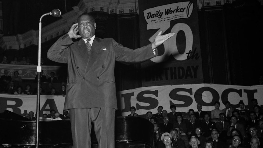 Paul Robeson singing on stage with banner behind says Daily Worker