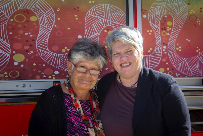 Two indigenous women posing in front of a fire truck with an indigenous motive on the side