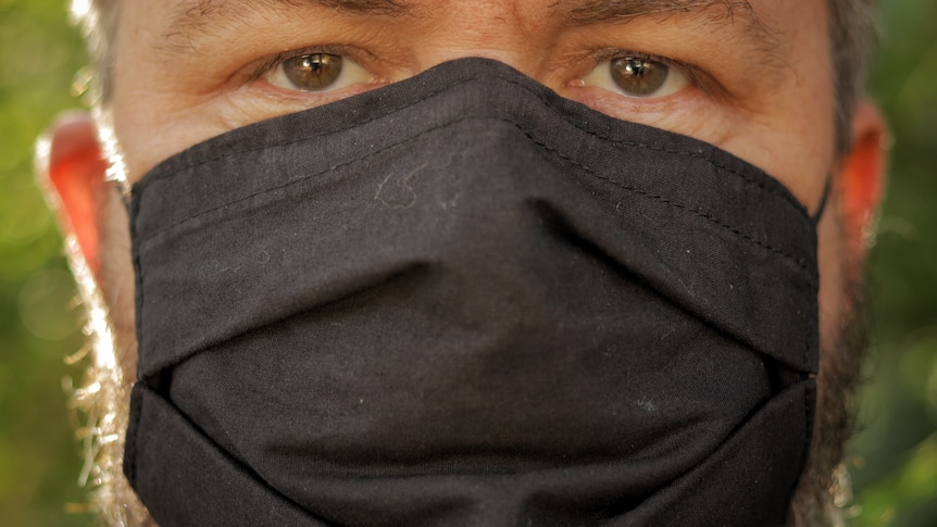 Close-up of man's face wearing a black face mask.