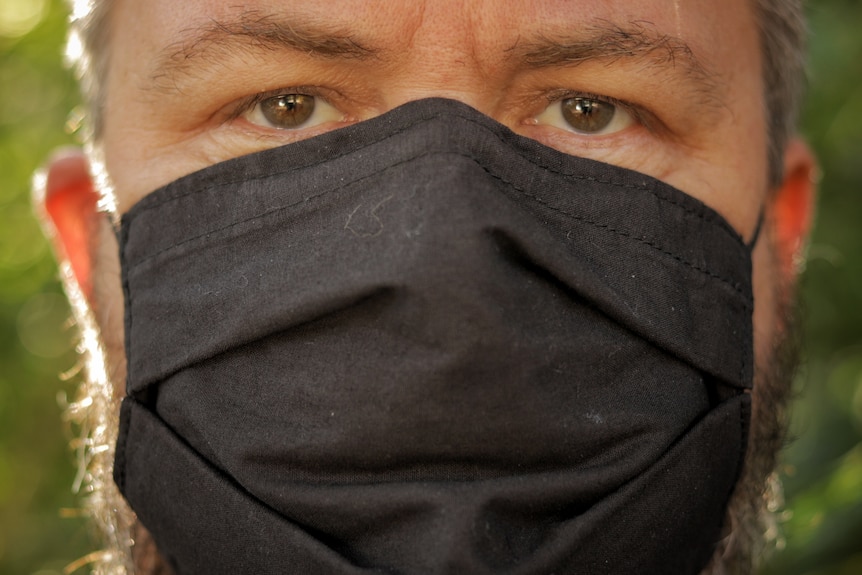 Close-up of man's face wearing a black face mask.