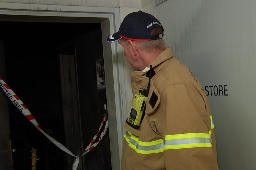 A firefighter looking into a dark room sectioned off with caution tape,
