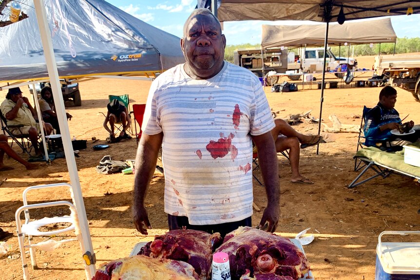 A man stands in behind slabs of meat displayed on an outside table