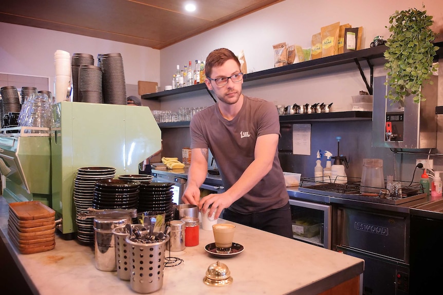 Ben glances towards a customer as he prepares a coffee