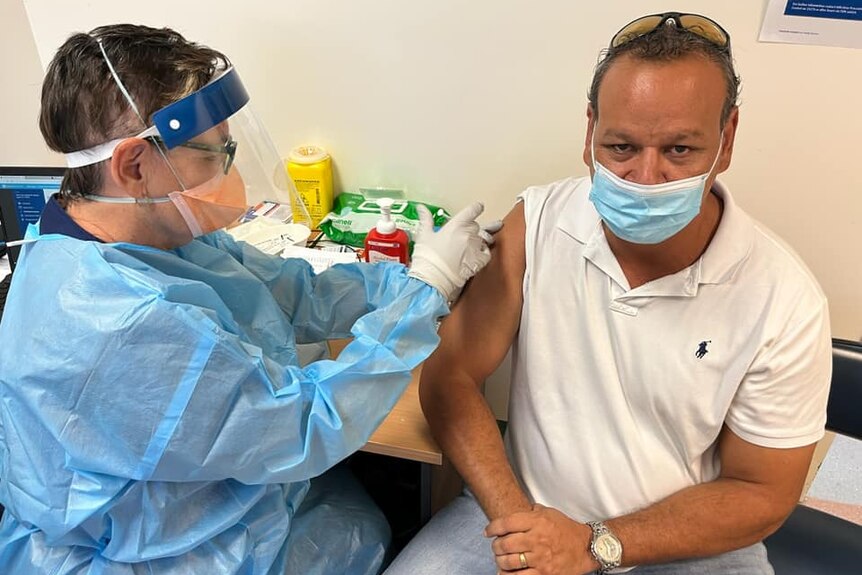 An indigenous man wearing a face mask is receiving a vaccinated in his right arm.