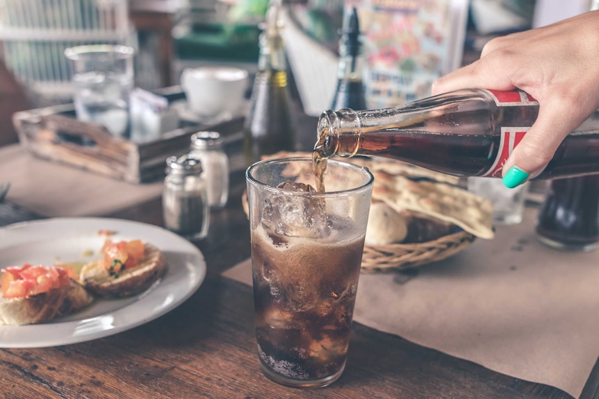 A hand pours a bottle of cola into a glass.